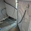 Rear view of a newly connected washing machine showing water inlet hoses and waste pipe plumbing hooked up to a valve