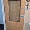 Damaged internal fire door with smashed reinforced safety glass window panel needing a full replacement on a commercial job