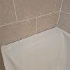 Deteriorating bathroom silicone sealant peeling away from white ceramic wall tiles prior to a fresh waterproofing repair