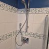 Weathered leaking shower handset and split metal hose hanging against bathroom tiles prior to a modern plumbing upgrade